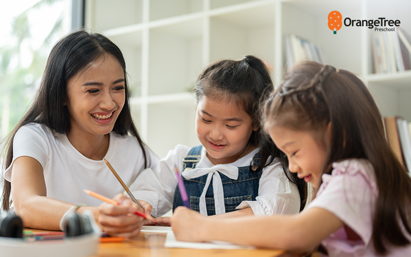OrangeTree Preschool teacher helping children with drawing.
