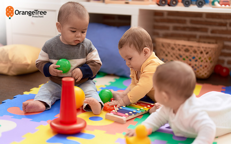 OrangeTree babies playing with toys on a mat.