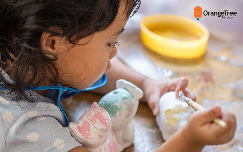 OrangeTree toddler painting ceramic figurines in art class.