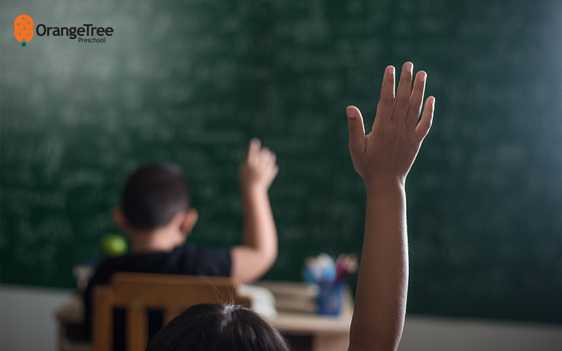 Preschool children raising hands in classroom.