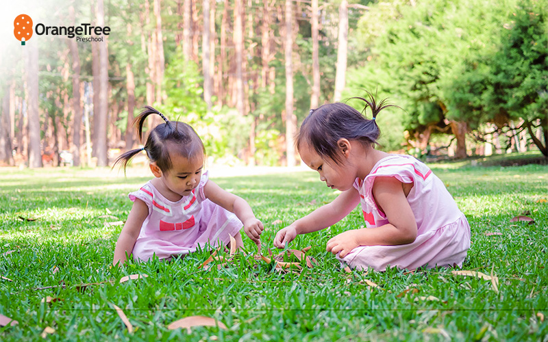 Two preschoolers playing in green grass outdoors.