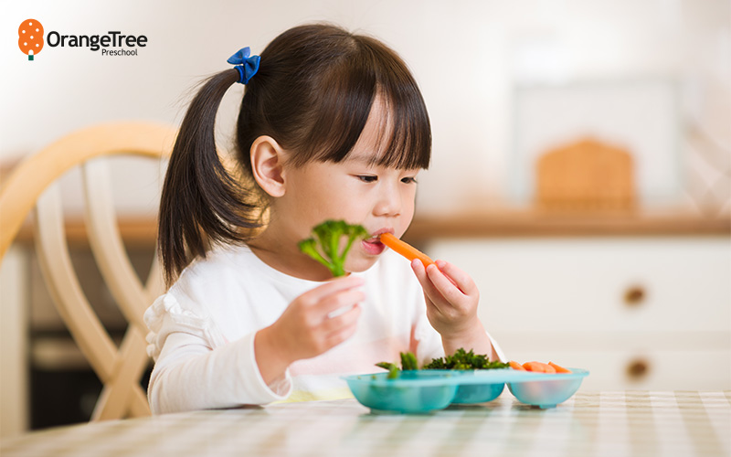 Young girl eating carrots and broccoli.